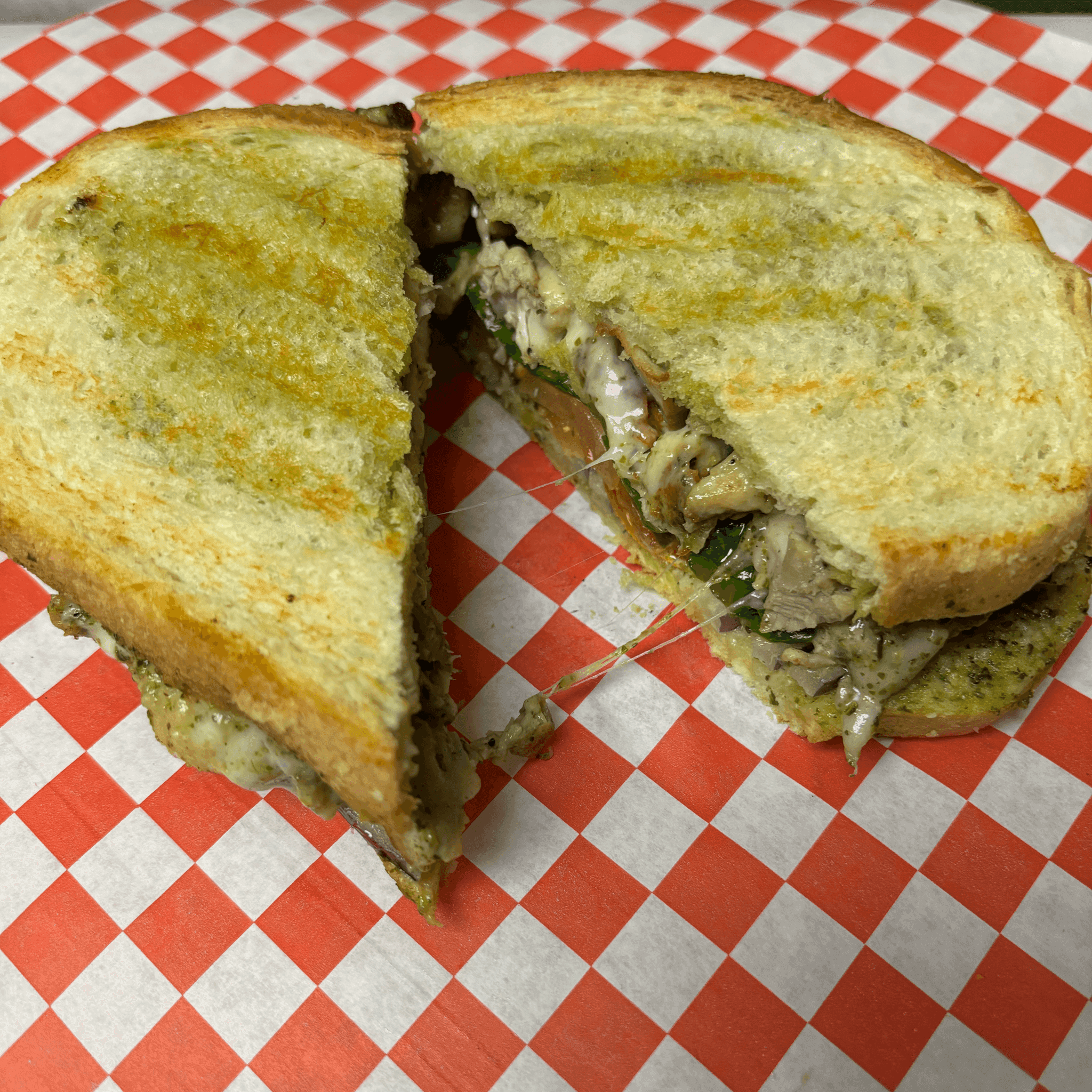 Toasted pesto panini cut in half on red checkered paper