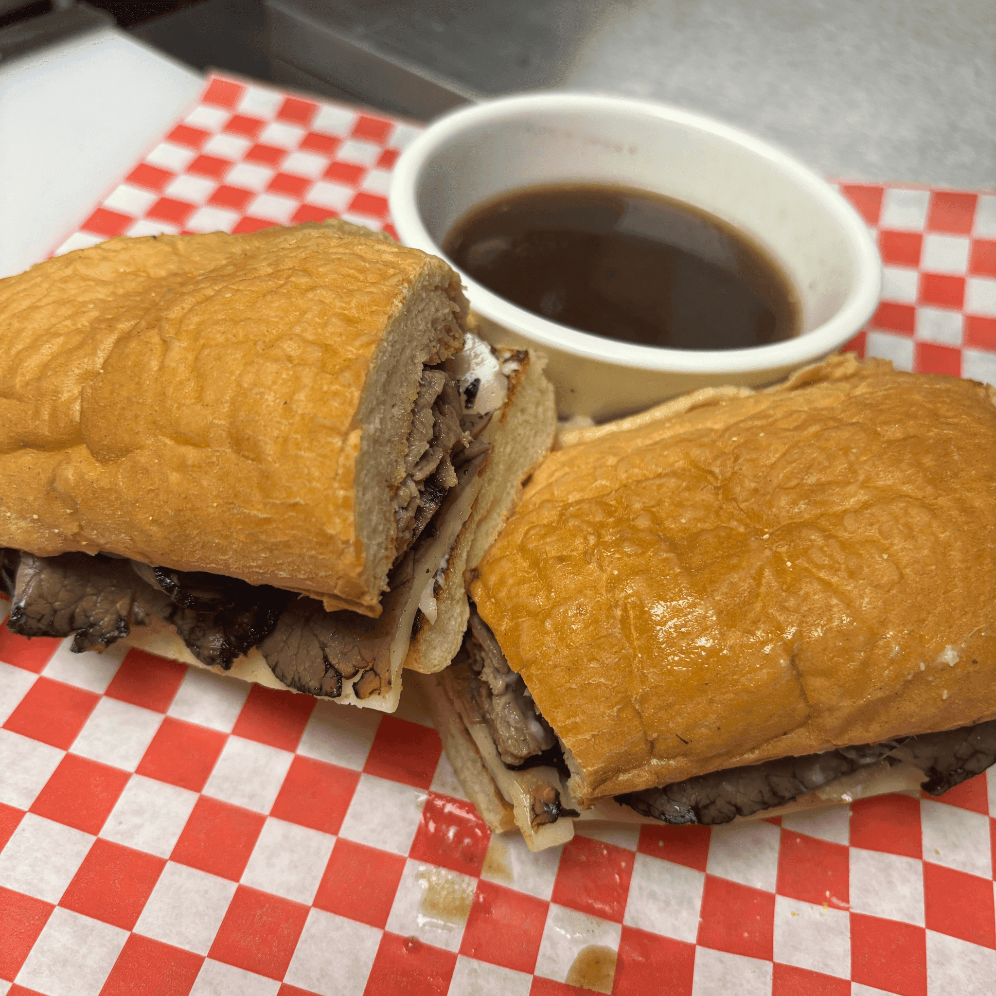 French dip sandwich on a roll with a cup of au jus for dipping