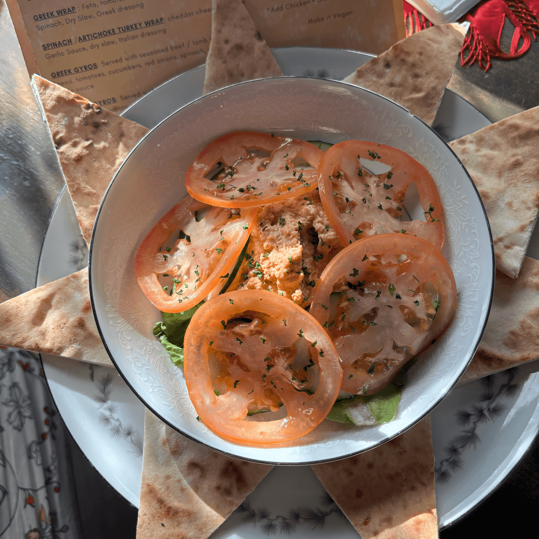 Bowl of hummus topped with tomato, surrounded by warm pita triangles